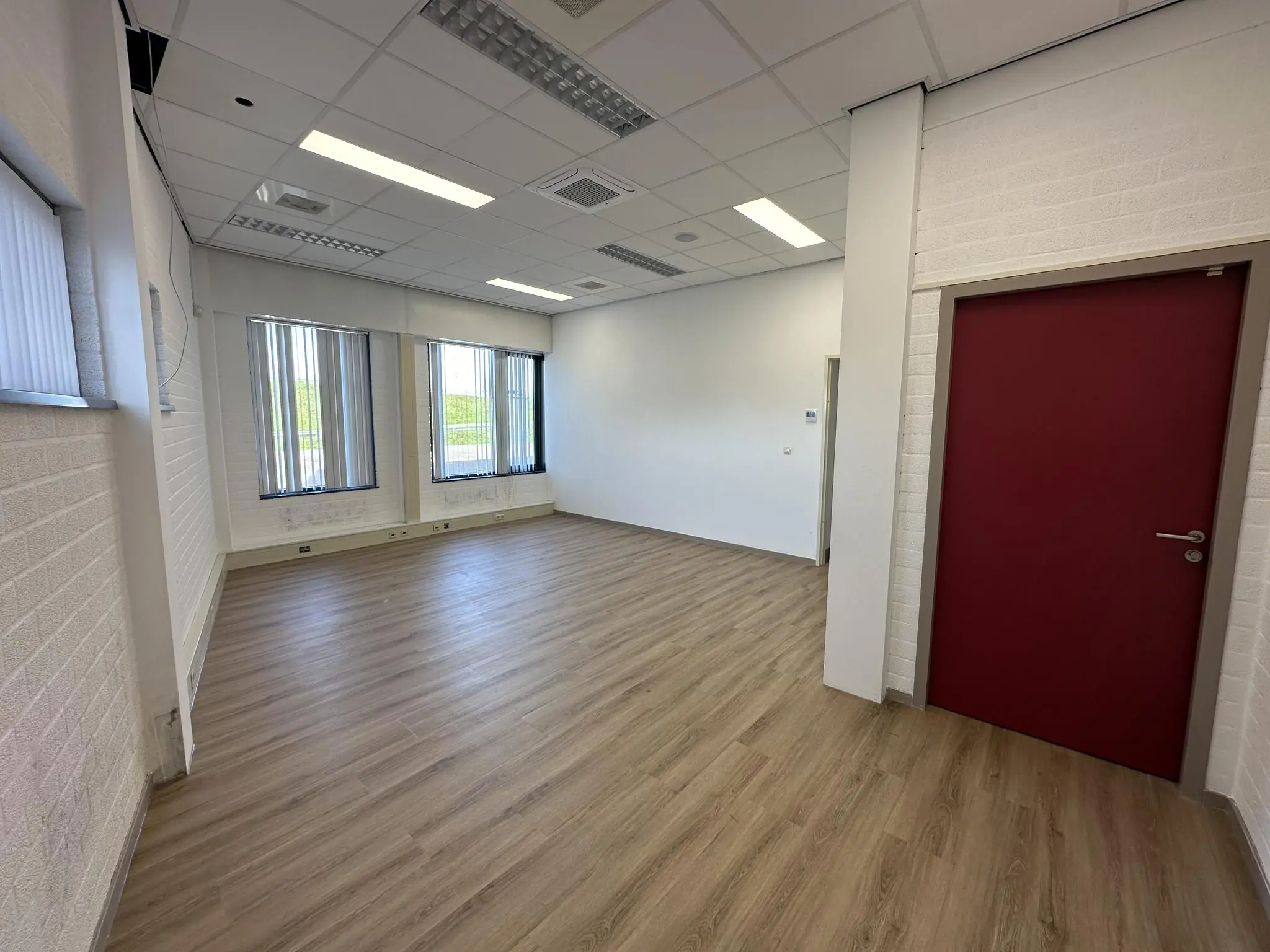 Leeg kantoorruimte met licht houten vloer, witte muren, systeemplafond en verticale jaloezieën aan de Van der Hagenstraat.